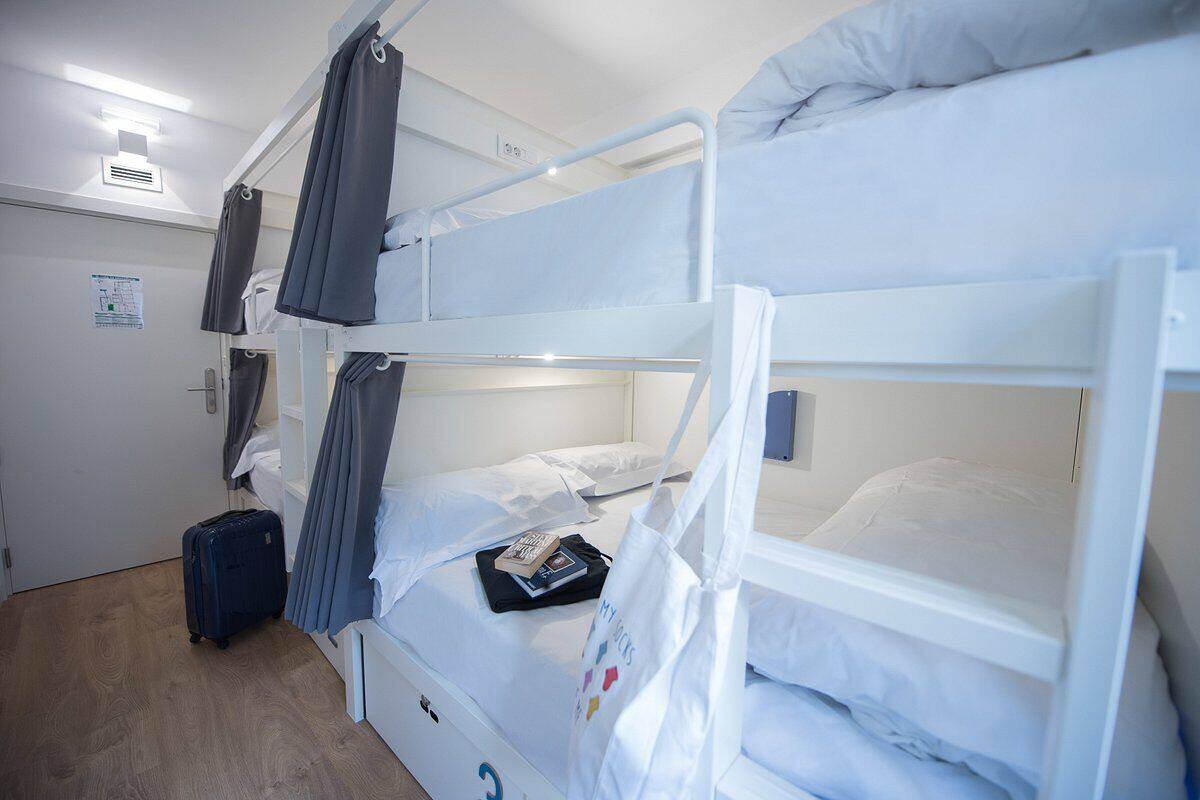 Habitación con literas, una maleta, un libro y un bolso en la cama inferior.