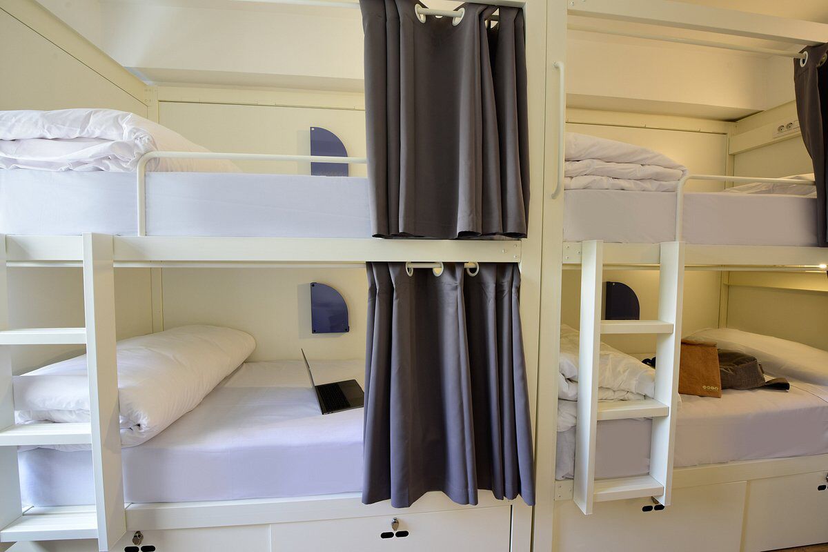 Une chambre avec un lit superposé, des rideaux, un ordinateur portable et une petite étagère.