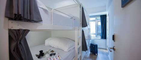 Une chambre avec un lit superposé, une fenêtre, une valise et une porte avec une pancarte.