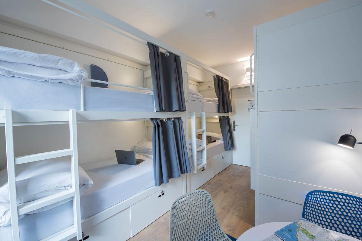 Un dormitorio con literas blancas, cortinas grises, un escritorio con silla y un mapa sobre la mesa.