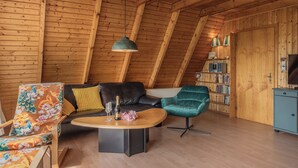 A cozy loft-style room with a wooden ceiling, a black leather sofa, a green velvet armchair, and a wooden coffee table. - Exceptional and unusual: The A-house with its ca. (Carolinensiel)