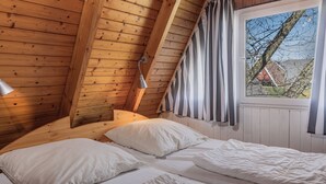 A bedroom with a sloped ceiling, wooden beams, a window with curtains, and a bed with white bedding. - Exceptional and unusual: The A-house with its ca. (Carolinensiel)