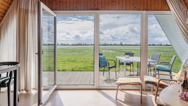 A room with a large sliding glass door leading to an outdoor deck with a table and chairs. - Exceptional and unusual: The A-house with its ca. (Carolinensiel)