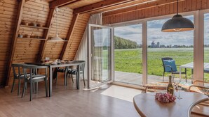 A dining area with a table and chairs, a large window with a view of a green field, and wooden ceiling beams. - Exceptional and unusual: The A-house with its ca. (Carolinensiel)