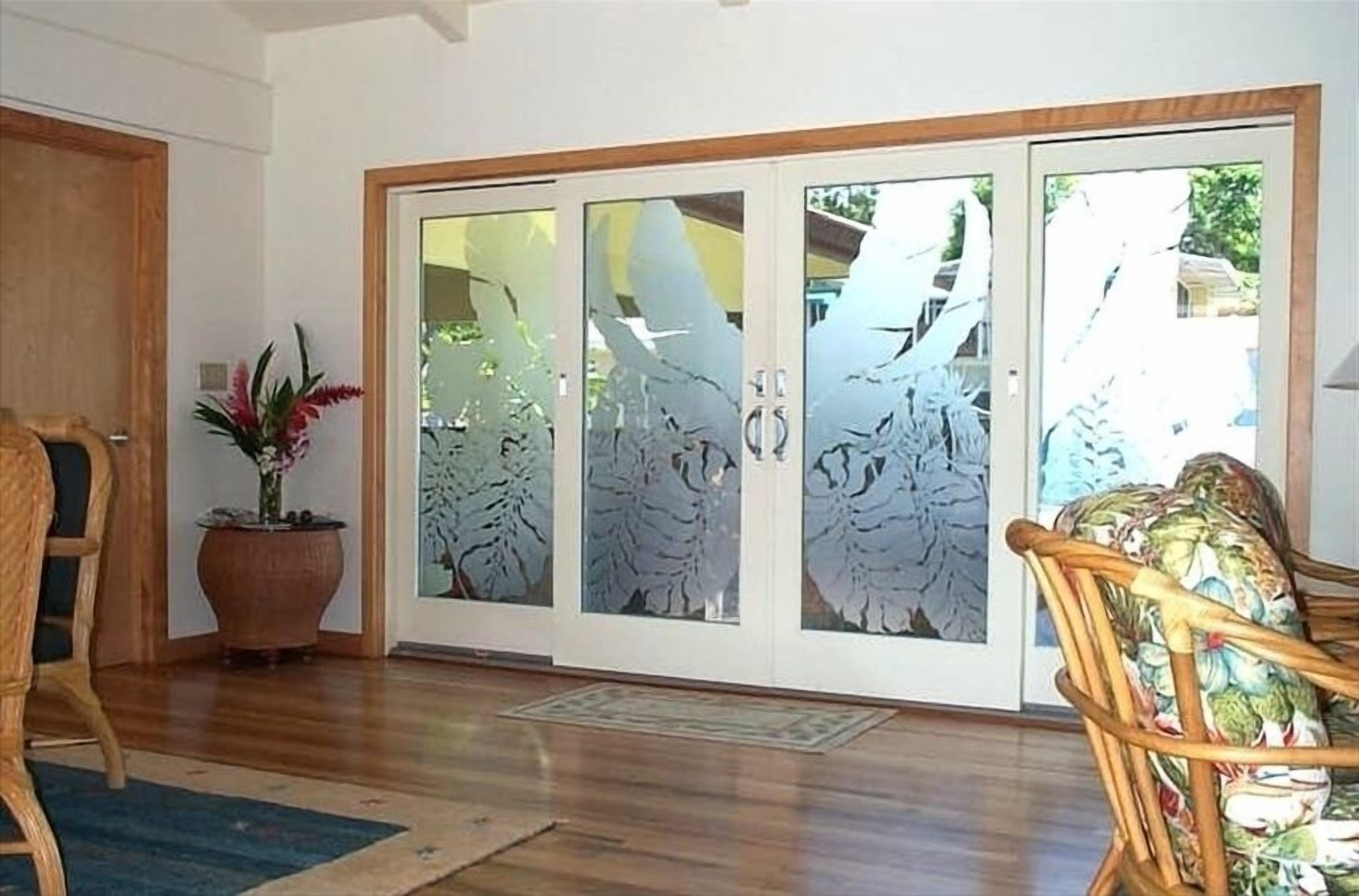 Une pièce avec un plancher en bois, une grande plante en pot, une chaise en osier et une porte en verre avec des panneaux en verre dépoli.
