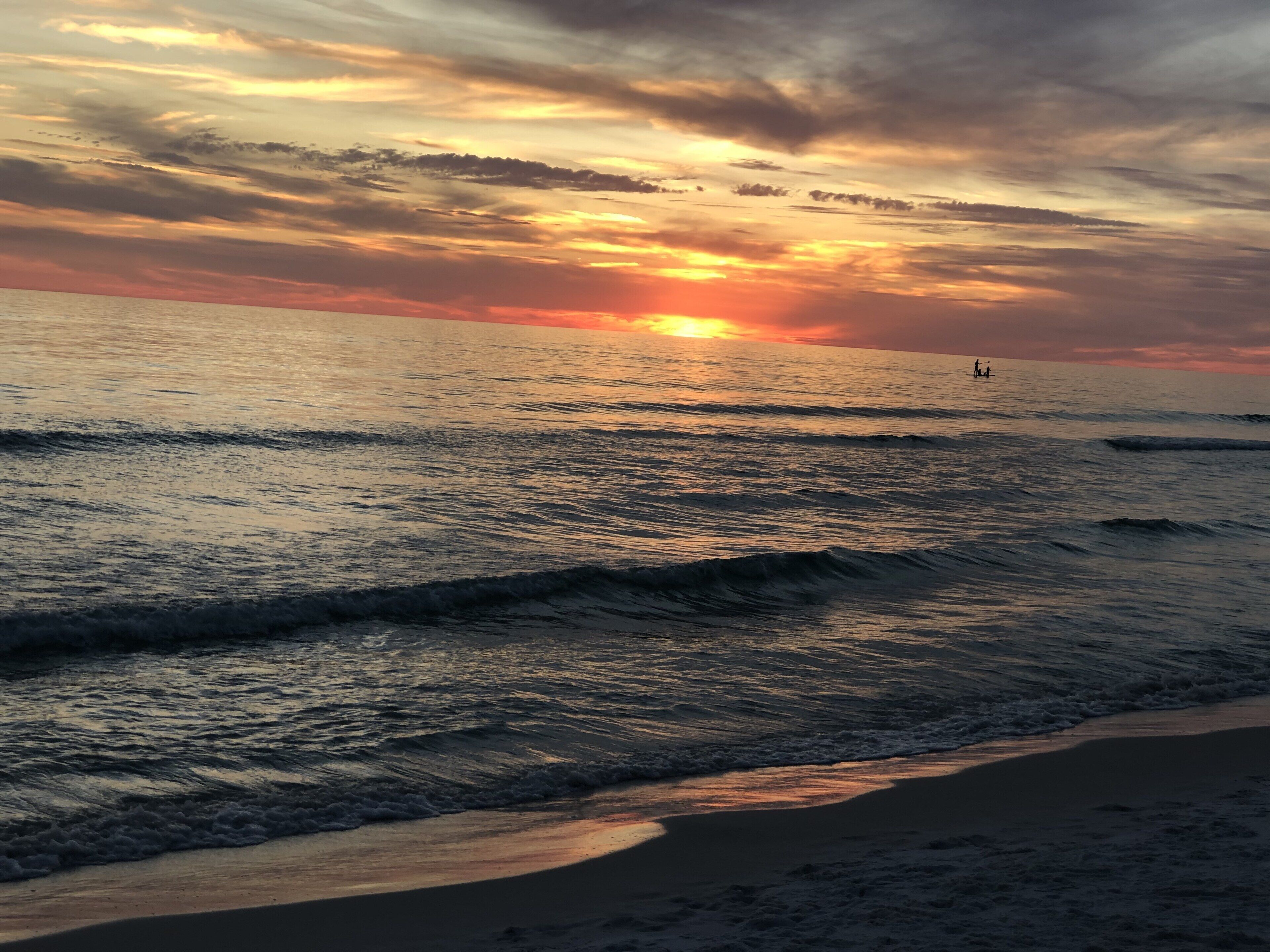 A beach at sunset with waves and a distant person on the water.