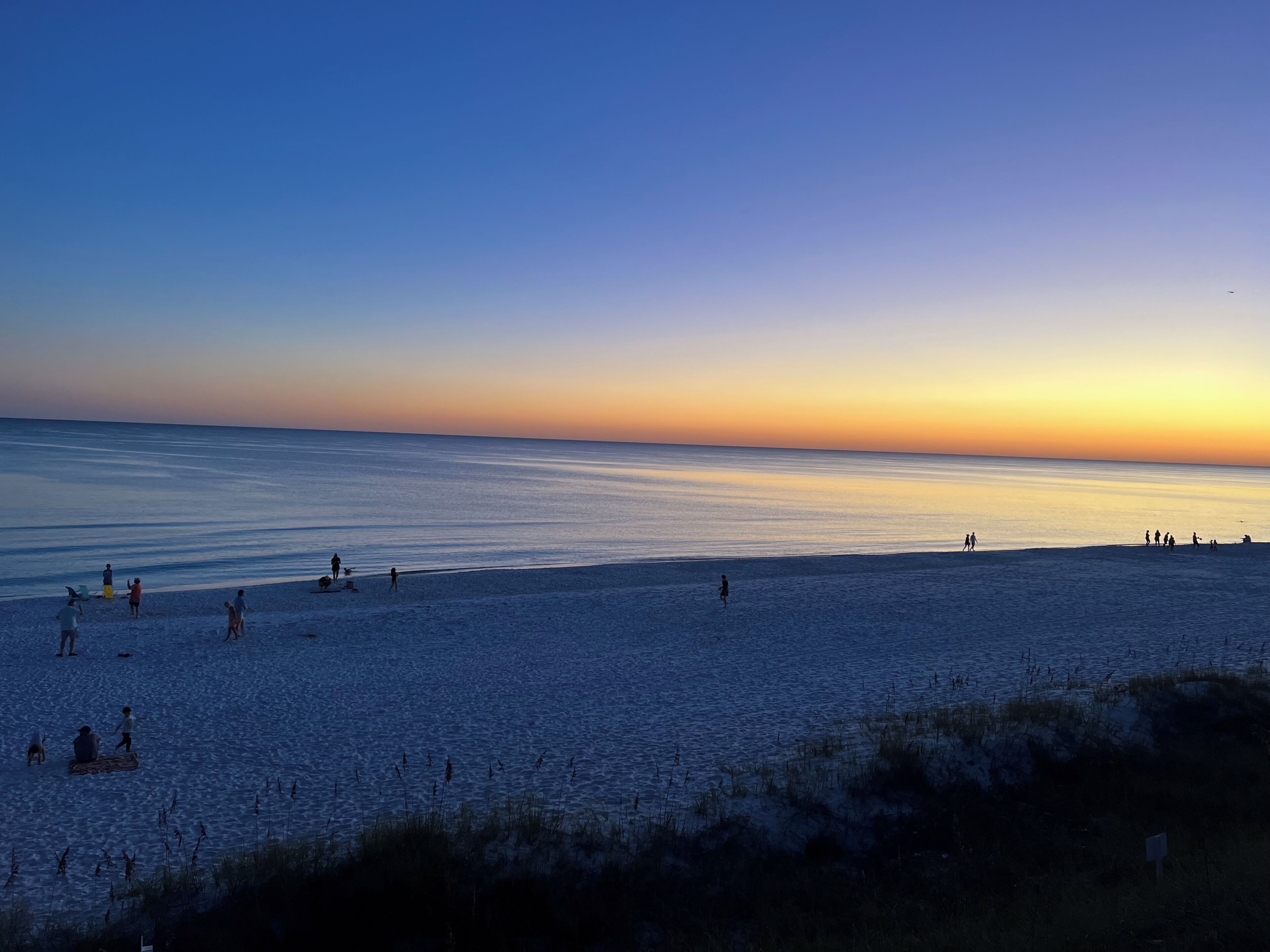 A beach with people walking and sitting, and a clear sky.