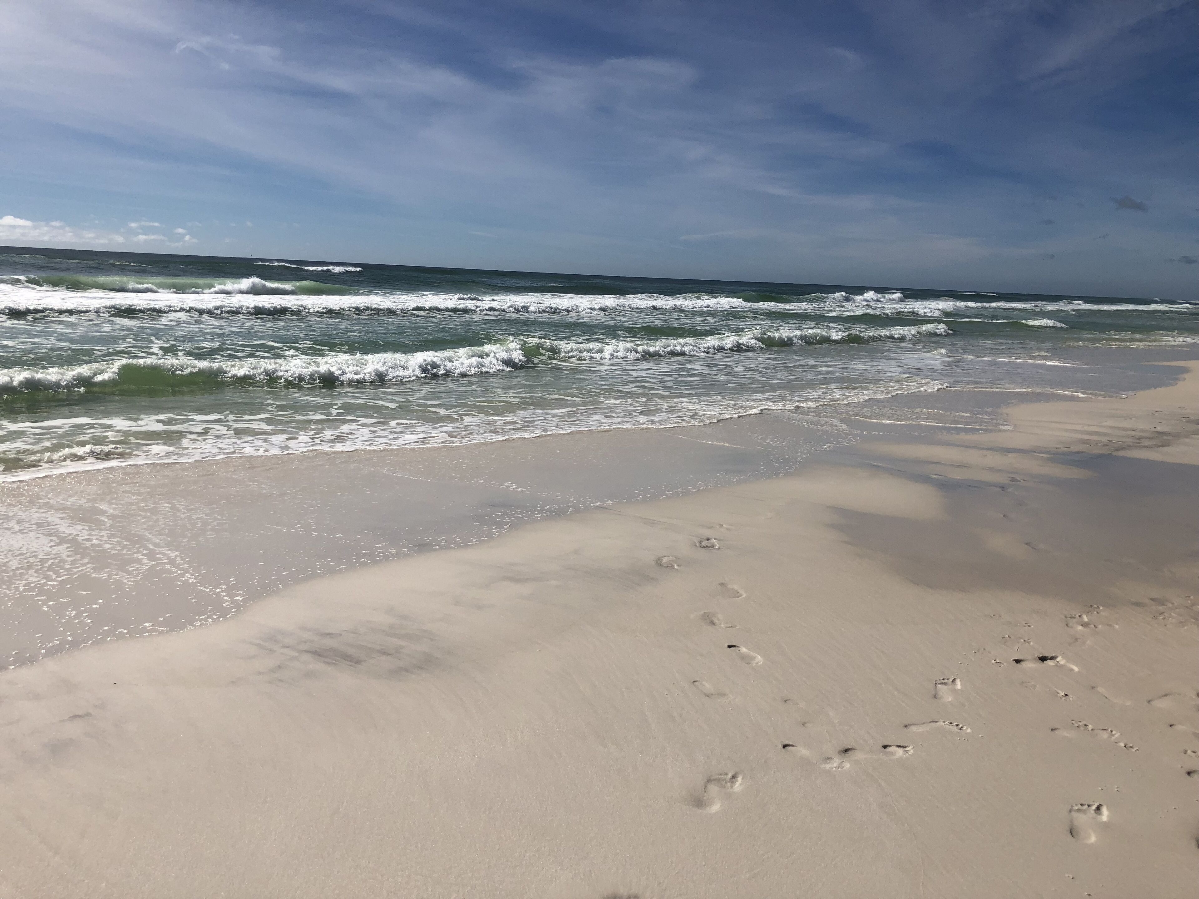 A beach with footprints in the sand and waves approaching the shore.