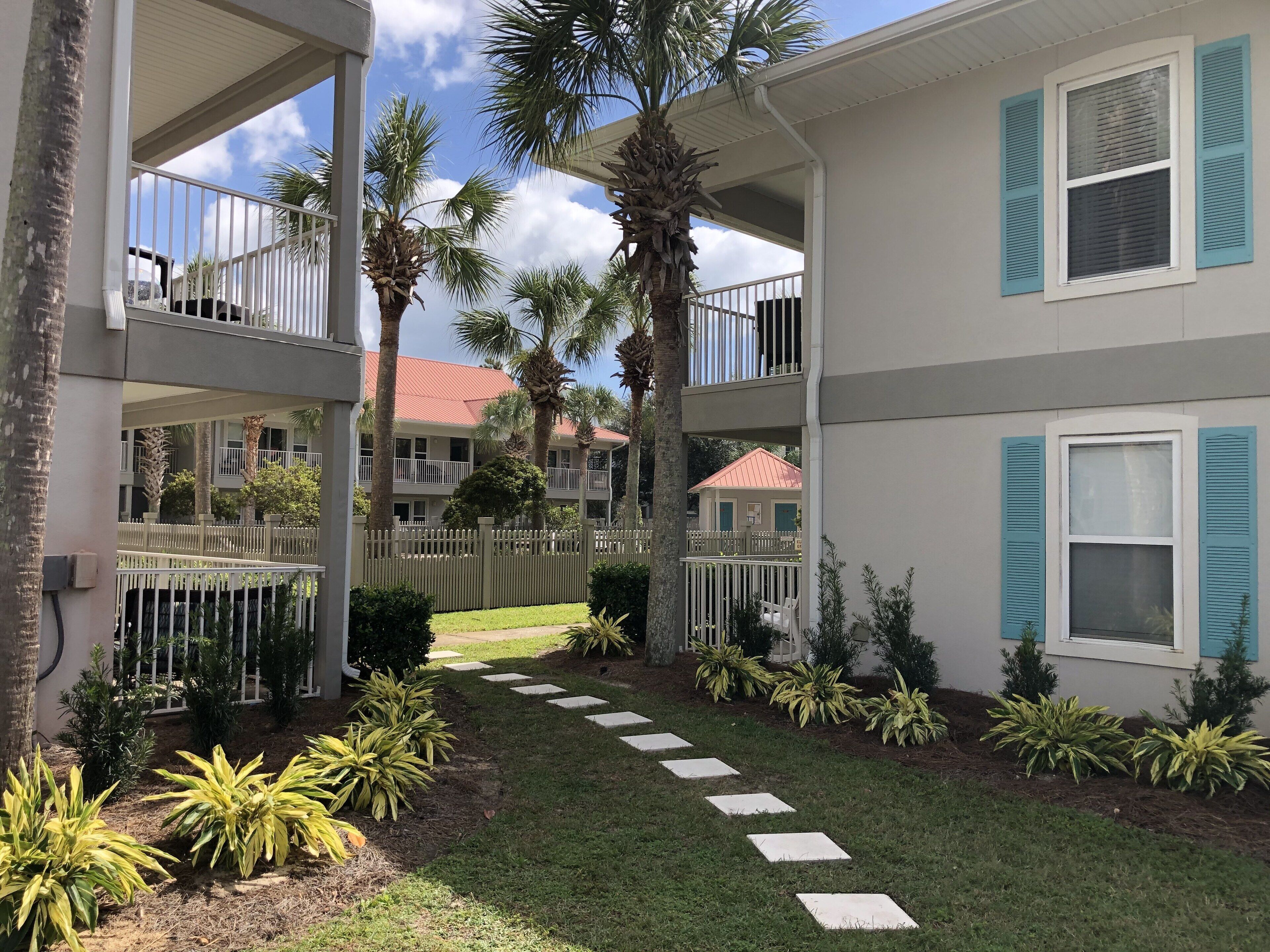 A multi-story building with balconies, a paved pathway, and palm trees.