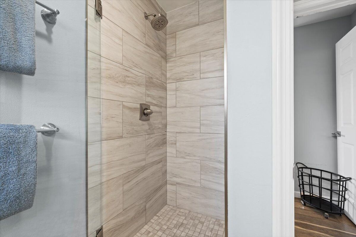 A bathroom with a shower, tiled walls, and a visible door leading to another room.