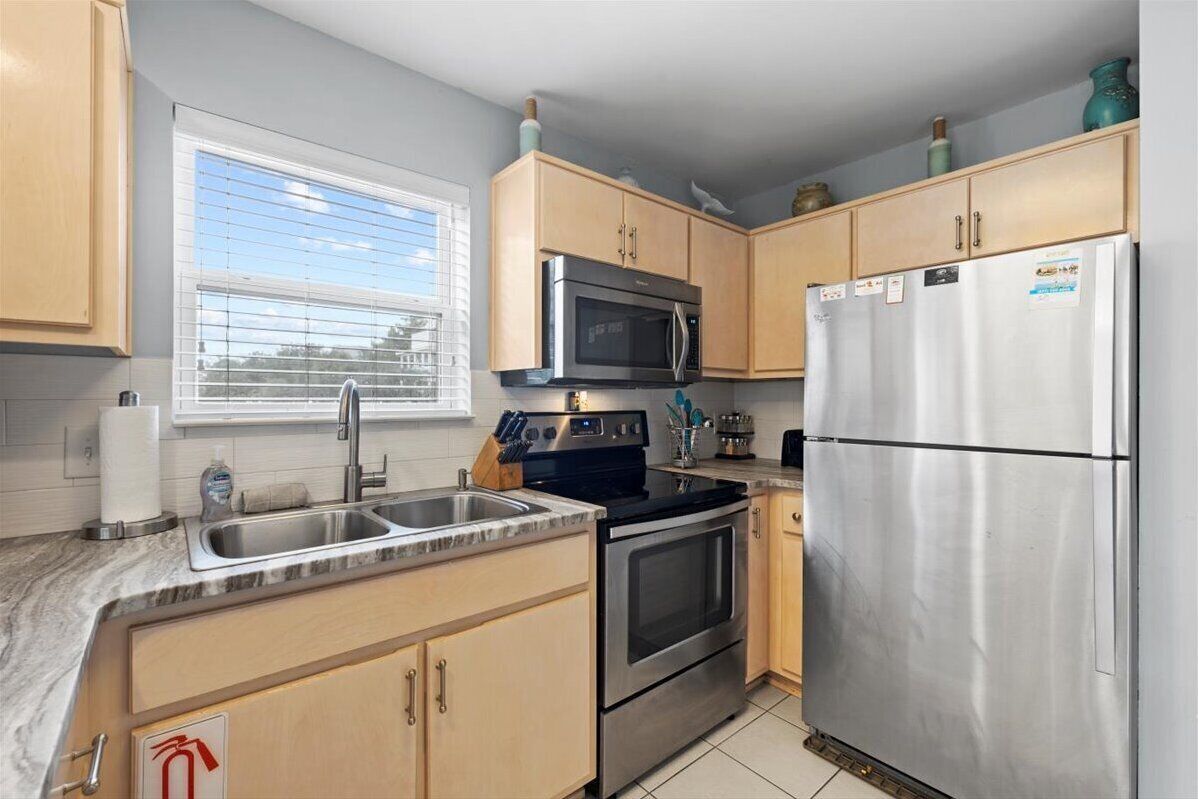 A kitchen with wooden cabinets, a stainless steel refrigerator, a microwave, an oven, and a sink.