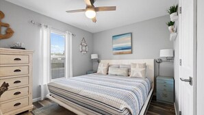 A bedroom with a bed, a dresser, a nightstand, a ceiling fan, and a window with curtains. - Modern coastal 1st floor 30A unit w/ walkability to restaurants & beach! (Santa Rosa Beach)