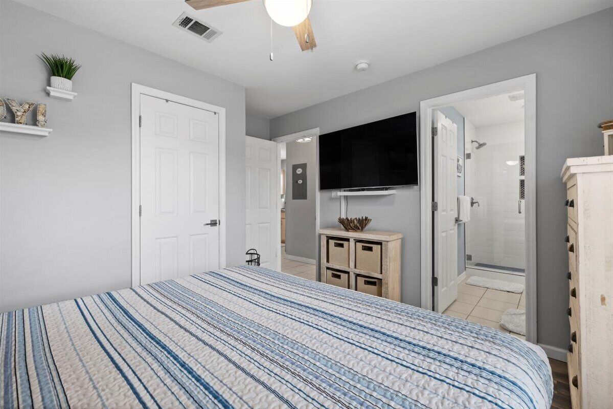 Un dormitorio con cama, televisión, ventilador de techo y puerta que da al baño.