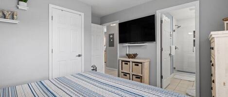 Un dormitorio con cama, televisión, ventilador de techo y puerta que da al baño.