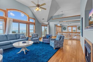A spacious living room with a blue carpet, a ceiling fan, and large windows offering a view of the sea. - Semi-Soundfront Home w/ Pool, Hot Tub, Elevator, Game Room, Community Boat Ramp (Salvo)