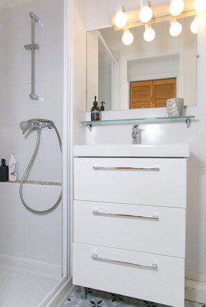 Une salle de bain avec une douche à parois de verre, un meuble-lavabo blanc doté de tiroirs et un miroir avec des lumières au-dessus.