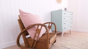 Une chaise à bascule en bois avec un coussin rose, une commode bleu clair avec des tiroirs et un tapis beige sur un plancher en bois.