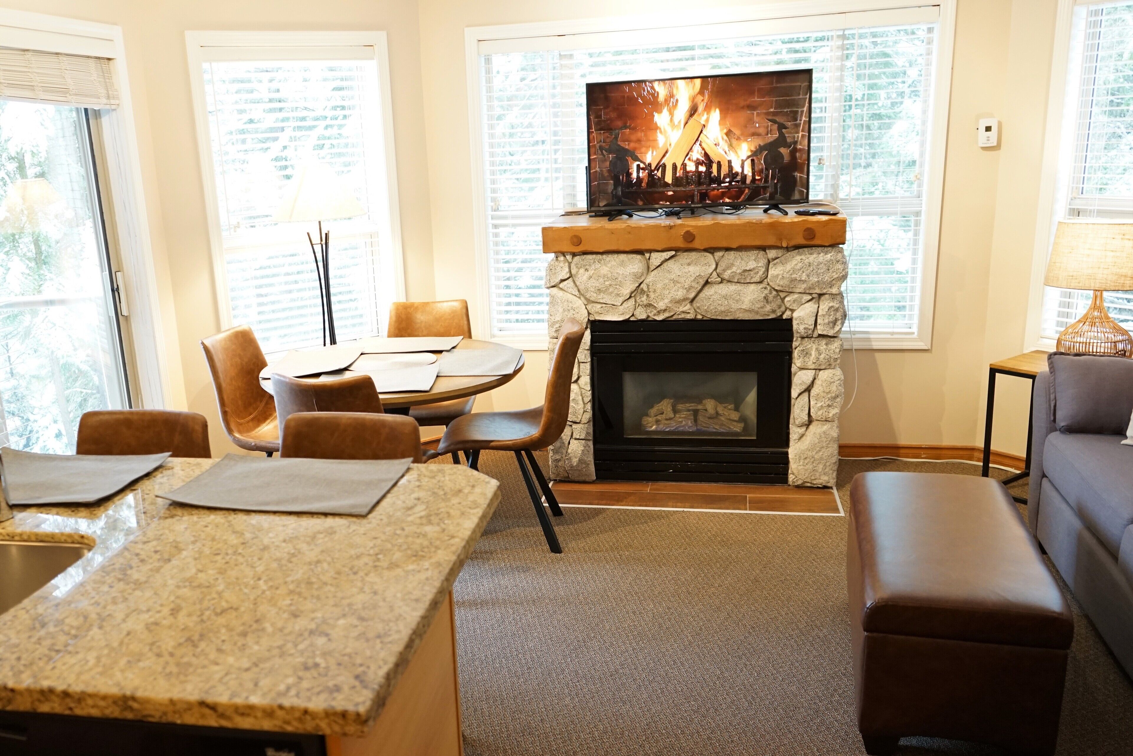 Una sala de estar acogedora con chimenea de piedra, un televisor montado encima y un comedor con mesa y sillas.