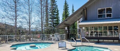 Un área de piscina con dos piscinas, un letrero con el nombre Aspen y un edificio con techo metálico.