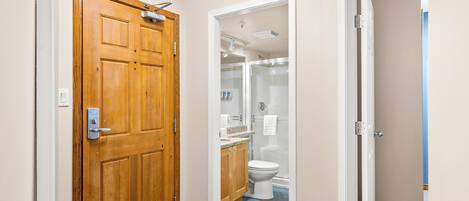A hallway leading to a bathroom with a wooden door, a white toilet, and a shower area.