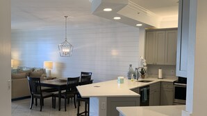 A modern kitchen with a central island, dark wooden chairs, a dining table, and a chandelier. - Enjoy Gorgeous Panoramic Views Of The Gulf Of Mexico And Vanderbilt Bay  (Naples)