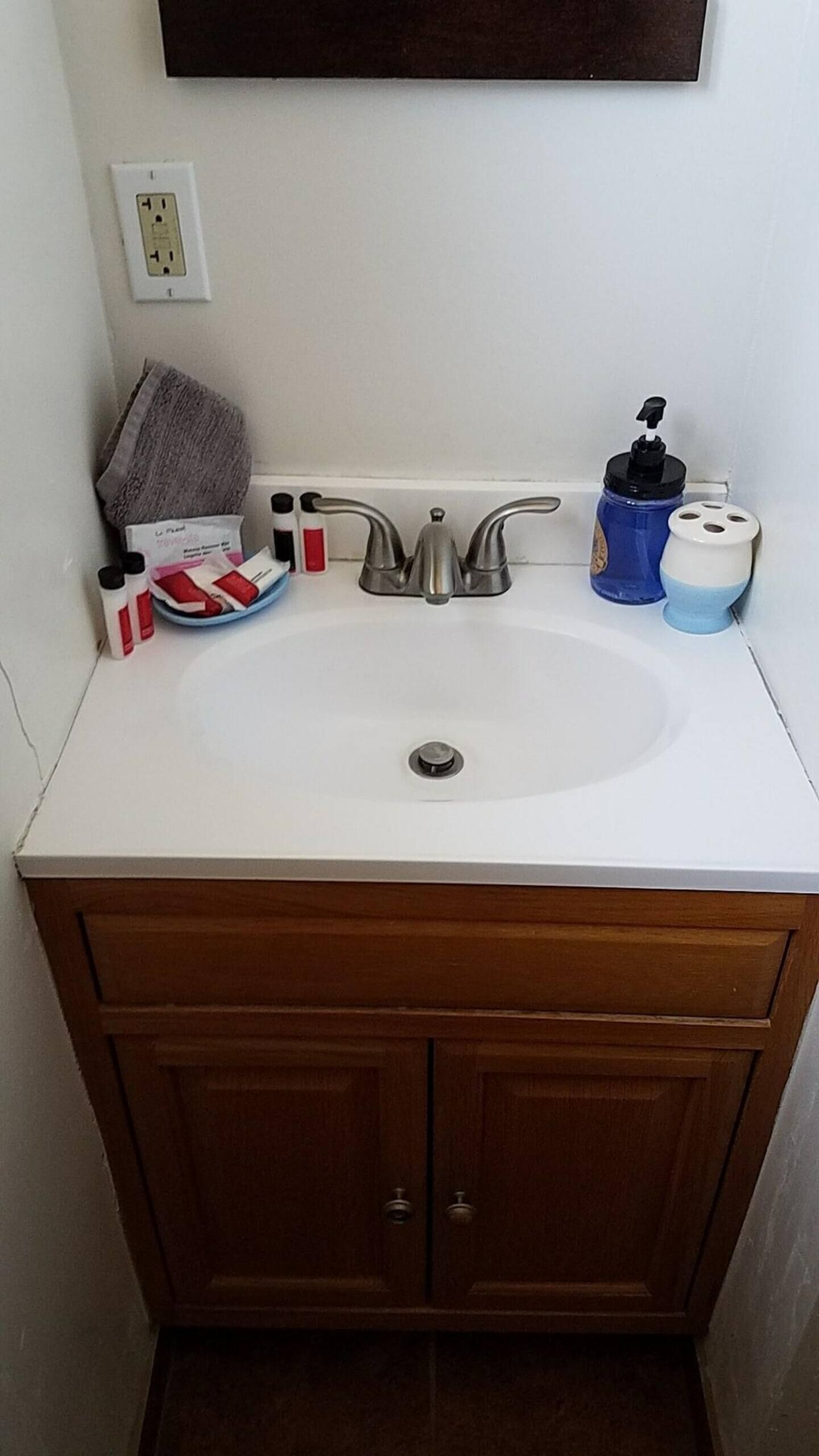 Une salle de bain avec un lavabo blanc, des meubles en bois, une serviette et des articles de toilette.