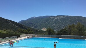A swimming pool with people, surrounded by mountains and trees.