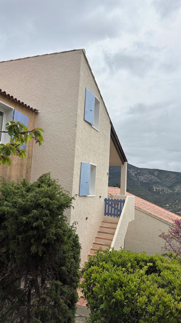A two-story building with a textured facade, a visible staircase, and a view of a mountainous landscape.