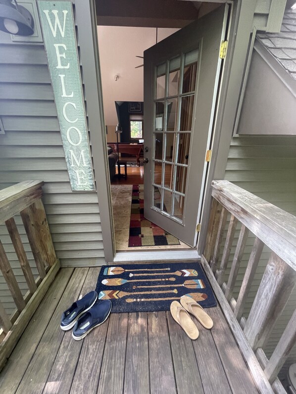 A wooden deck with a welcome mat and shoes, a door leading inside, and a 'WELCOME' sign.