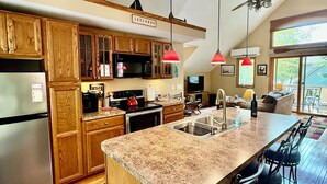 A modern kitchen with wooden cabinets, a granite countertop, a built-in stove, and a large island with bar stools. -  Cozy, waterfront getaway for 2, w/loungers for relaxing & enjoying the sunsets (Lake Leelanau)