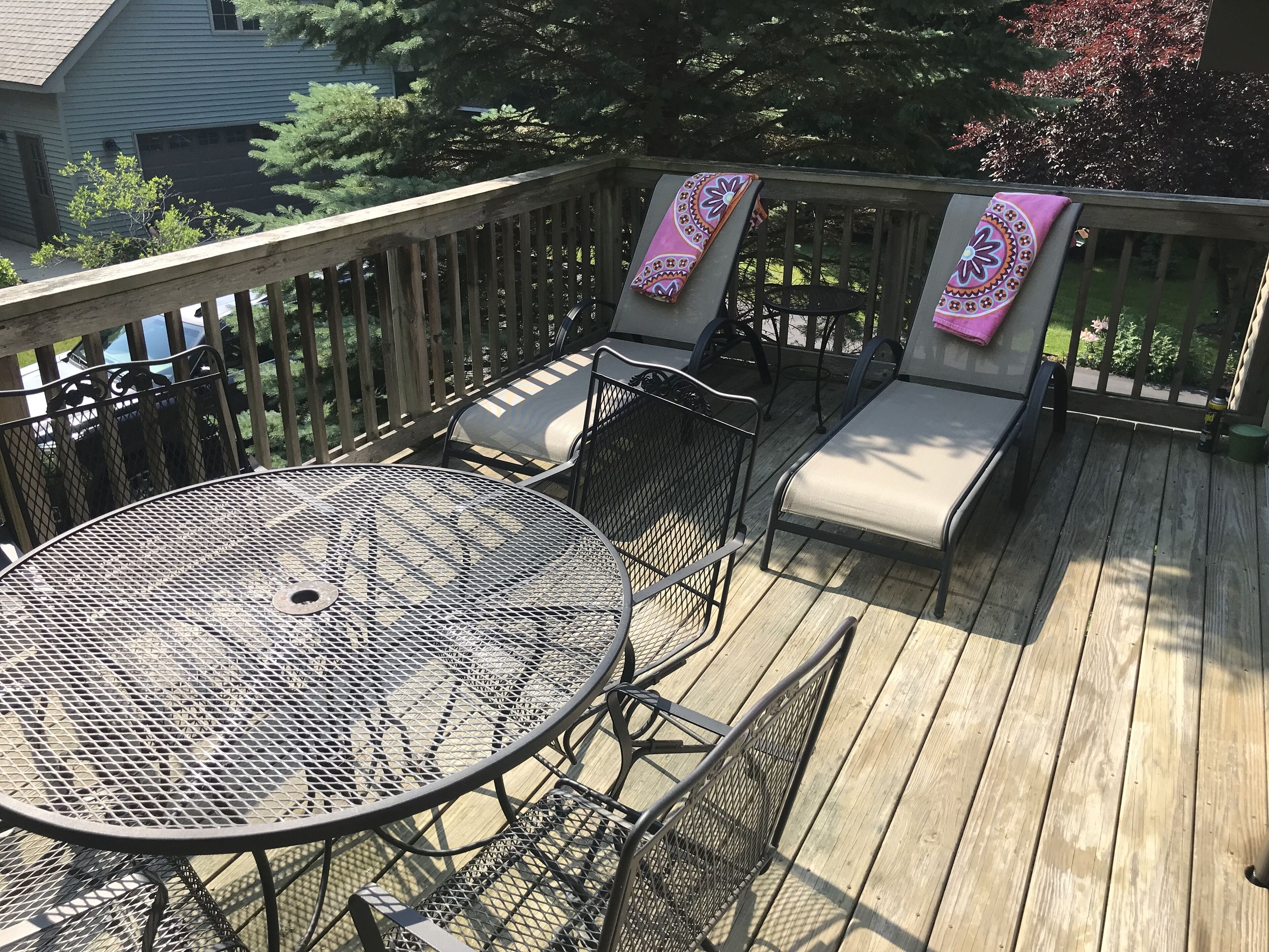 A wooden deck with a round metal table and two cushioned chairs, each with a pink patterned cloth.
