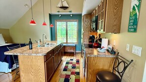 A kitchen with wooden cabinets, a central island, and a colorful rug. -  Cozy, waterfront getaway for 2, w/loungers for relaxing & enjoying the sunsets (Lake Leelanau)