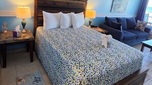 A bedroom with a bed, a nightstand, a bedside table, a blue sofa, and a wall with framed pictures. - Brandy's Direct Ocean View Over The Large Heated Pool & Hot Tub, Sleeps 4 (Daytona Beach)