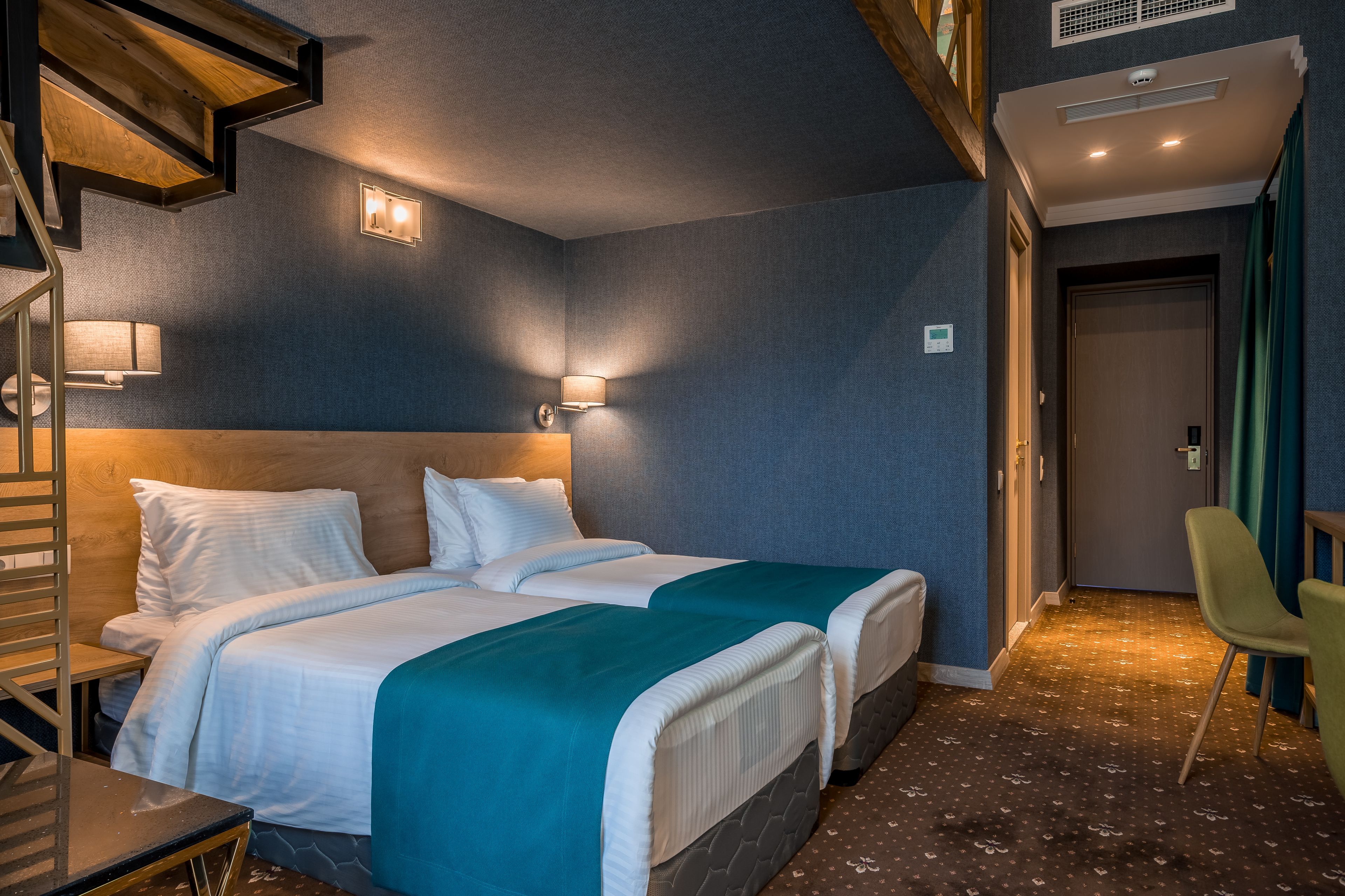 A hotel room with two beds, a wooden staircase, a desk, and a chair.