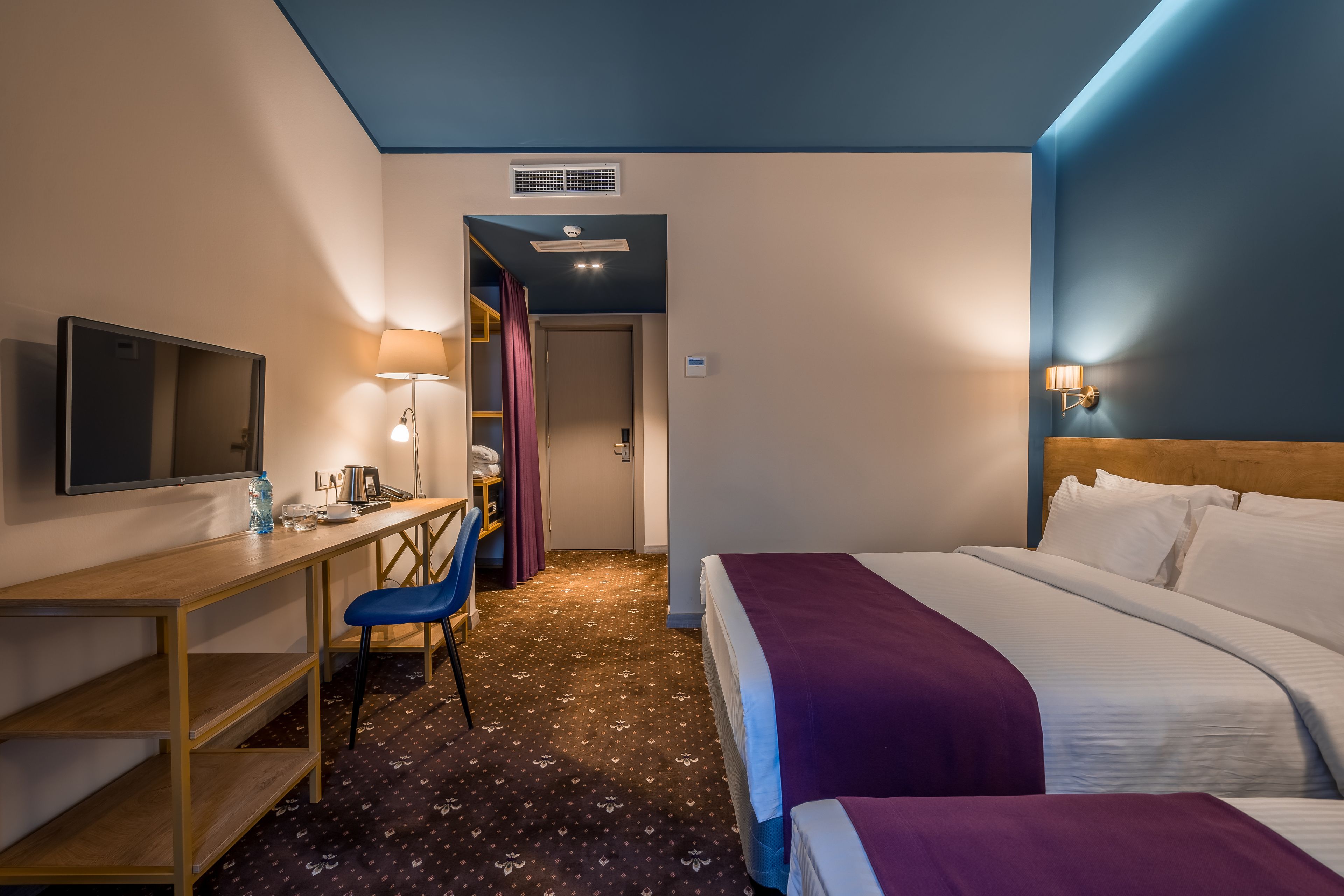 A hotel room with a bed, a desk, a chair, a TV, and a lamp.
