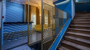 A modern staircase with a geometric railing design, a blue and white striped wall, and a wooden floor. - Hotel Gladius inn (Tbilisi)