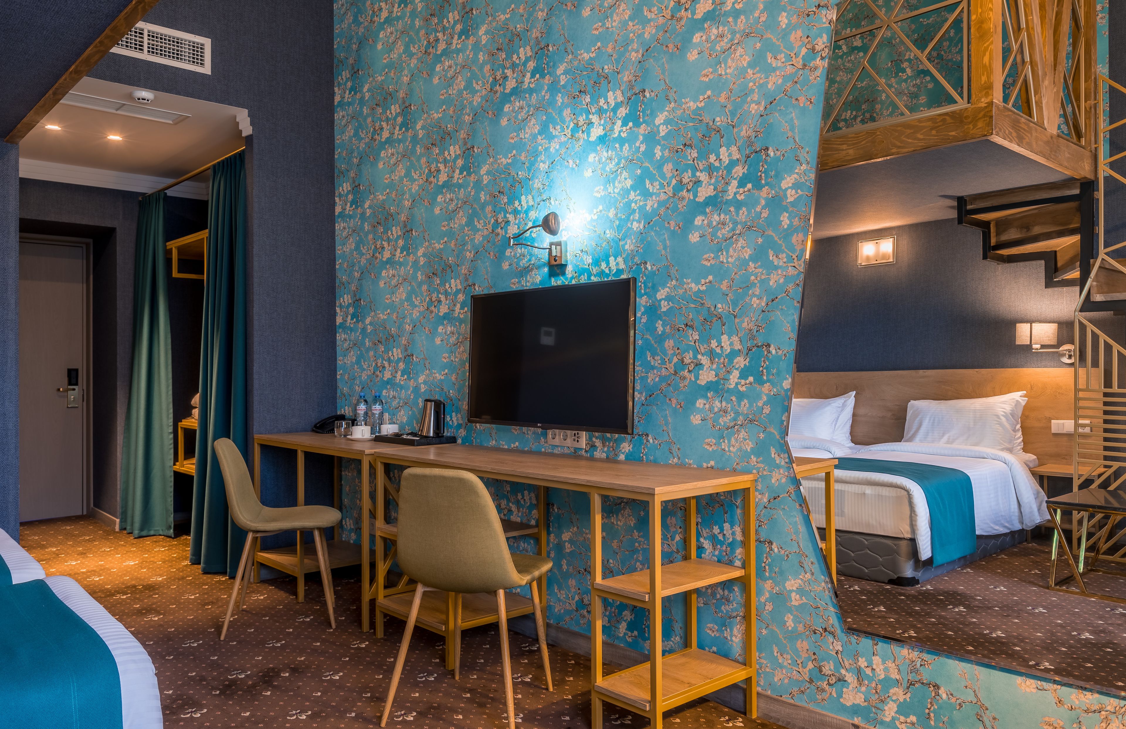 A hotel room with a desk, two chairs, a bed, and a TV.