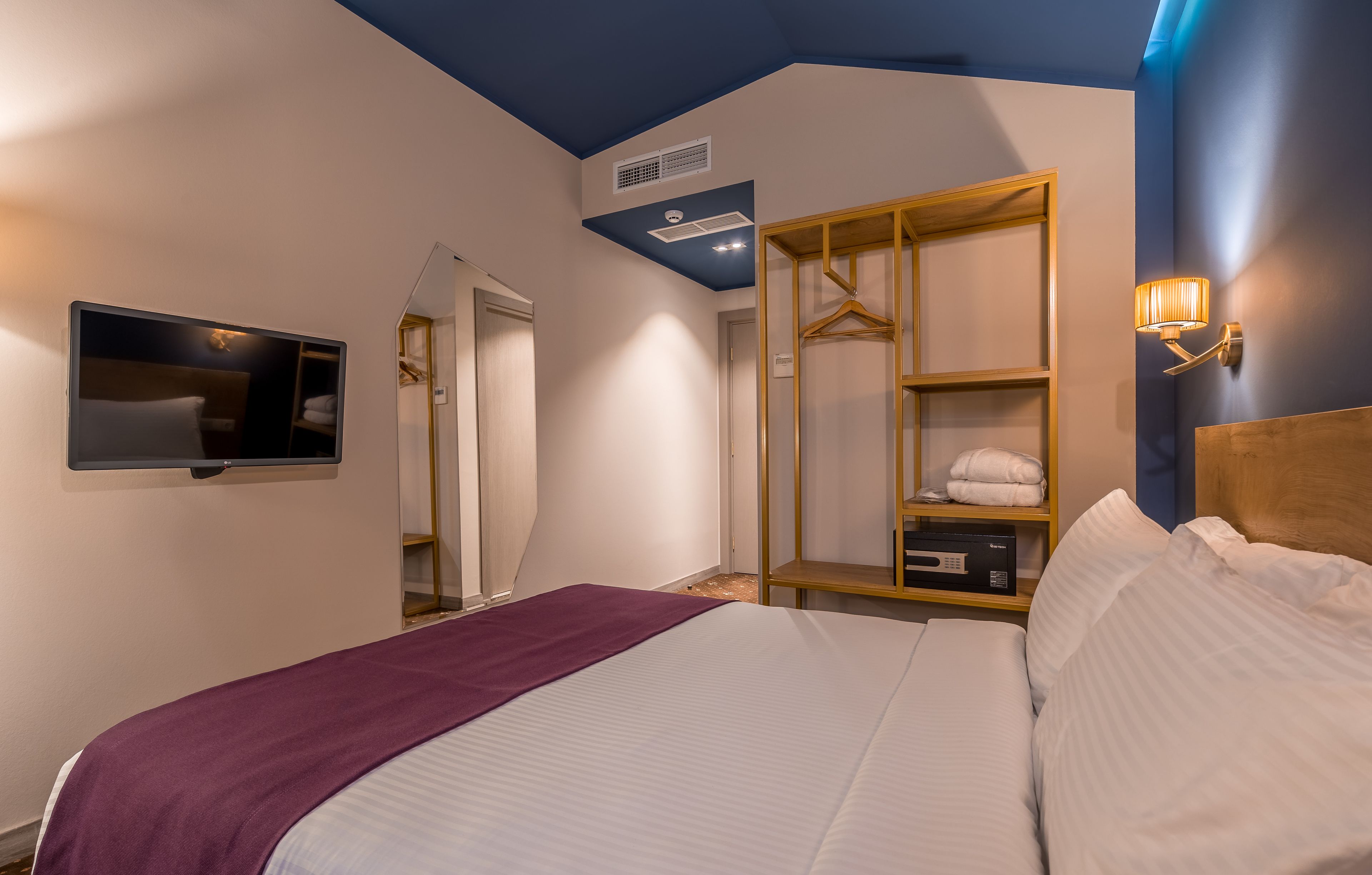 Une chambre à coucher comprenant un lit, un téléviseur fixé au mur, une armoire et une table de chevet avec une lampe.