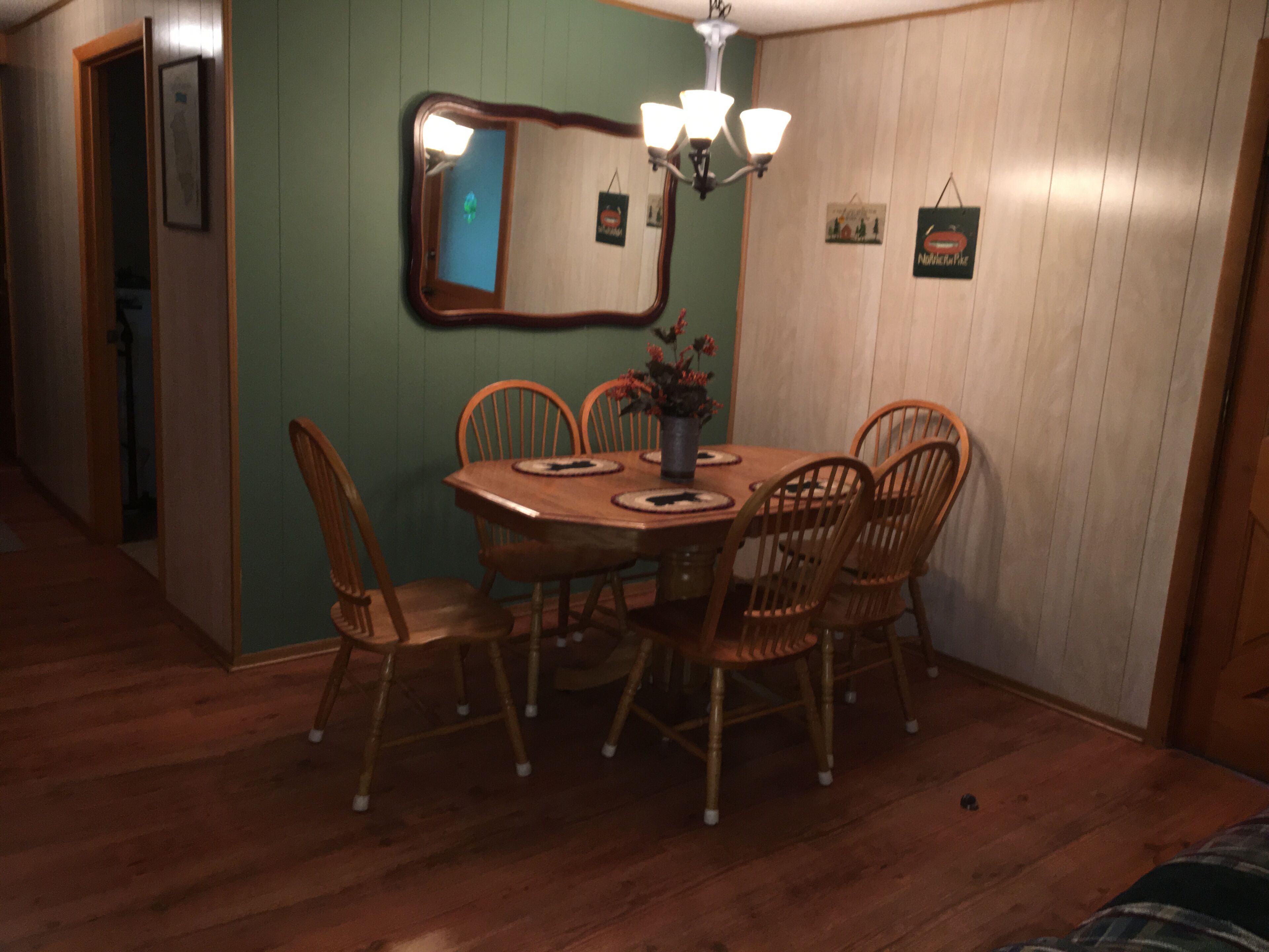 A dining area with a wooden table and chairs, a chandelier, and a mirror on the wall.
