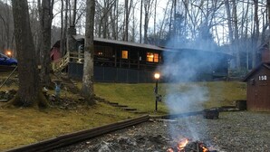 A rustic cabin with a fire pit in the foreground, surrounded by trees and a wooden deck. -  Pet friendly , Motorcycle parking  Hot tub. Close to everything (Maggie Valley)