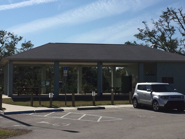 A covered parking area with a car parked inside, a wheelchair-accessible sign, and a building with a flat roof in the background. - IMAGINE THIS! EASY WALK TO THE BEACH-MERE STEPS TO LAGOON BEHIND PROPERTY (New Smyrna Beach)