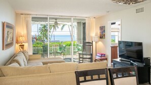 A living room with a sofa, a TV, and a balcony with a view of the ocean.
