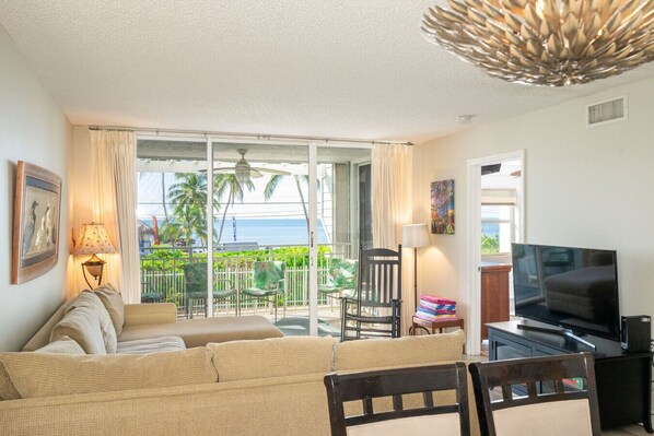 A living room with a sofa, a TV, and a balcony with a view of the ocean.