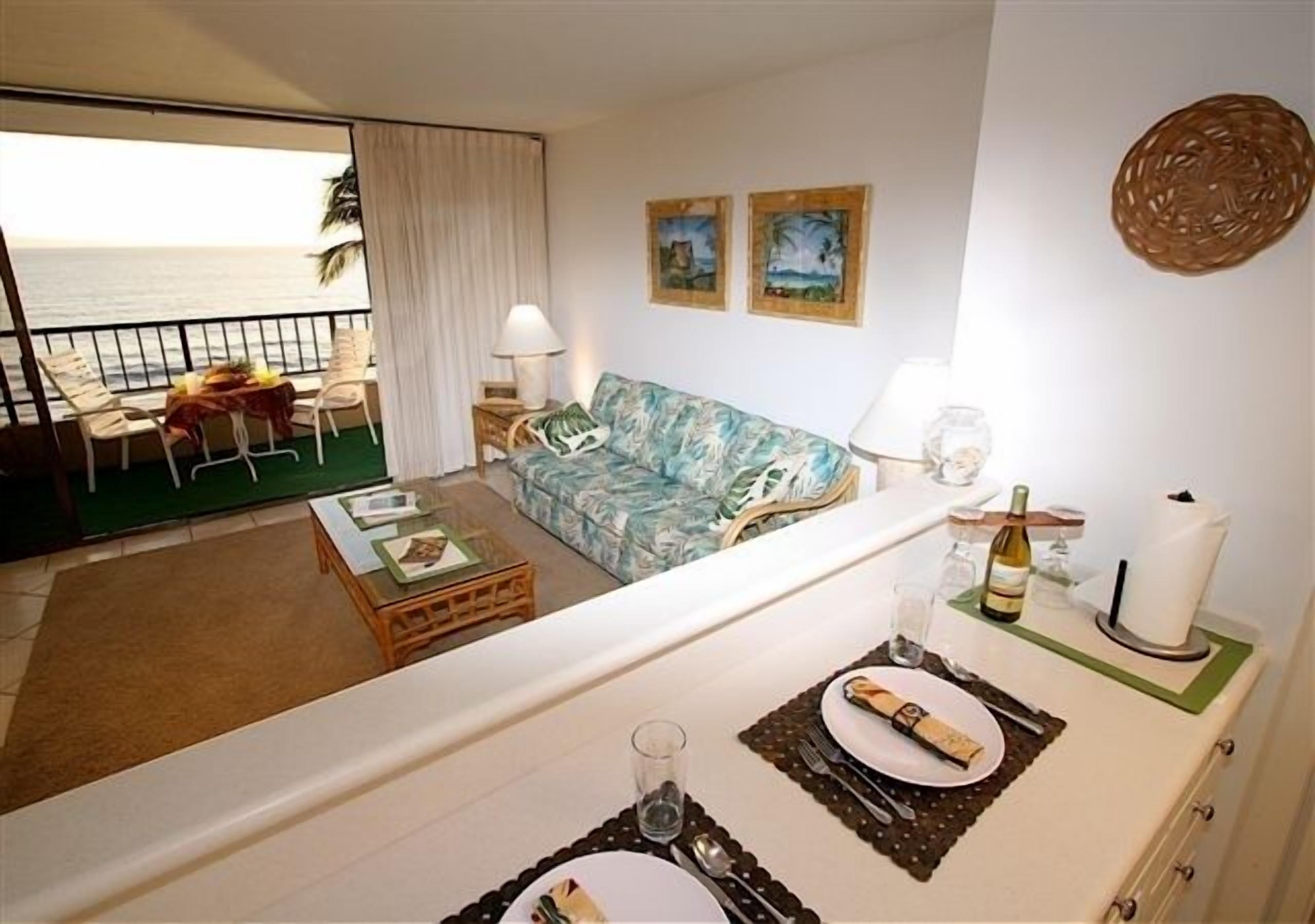 Una sala de estar con un sofá, una mesa de comedor preparada para dos personas y vista al océano desde un balcón.