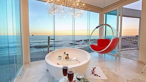 Une salle de bain moderne avec une grande baignoire, un fauteuil suspendu et une vue sur l’océan.