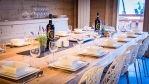 Een lange eettafel gedekt met witte borden, kommen en wijnglazen, omringd door witte stoelen.