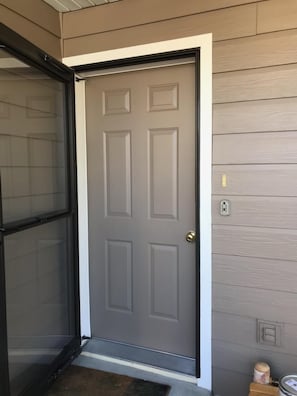 A closed grey door with a white trim, a black-framed window to the left, and a light switch on the wall to the right.