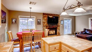 A kitchen with a brick fireplace, a dining area with wooden chairs and a red tablecloth, and a leather sofa in a living room. - Anglers Rest (Oakhurst)
