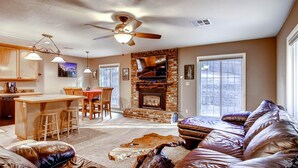 A spacious living room with a leather sofa, a fireplace, and a dining area with wooden furniture. - Anglers Rest (Oakhurst)