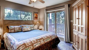 A bedroom with a large bed, a ceiling fan, a window with curtains, and a view of the outdoors. - Anglers Rest (Oakhurst)